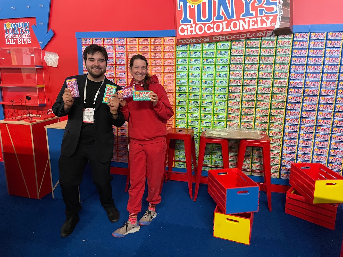 Stephen at the Tony's Chocolonely booth at Natural Foods Expo West, holding bars in front of a full wall of chocolate