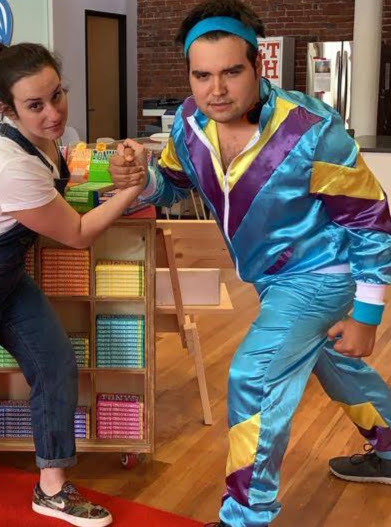 Stephen in a shiny tracksuit mock arm-wrestling a colleague in the office